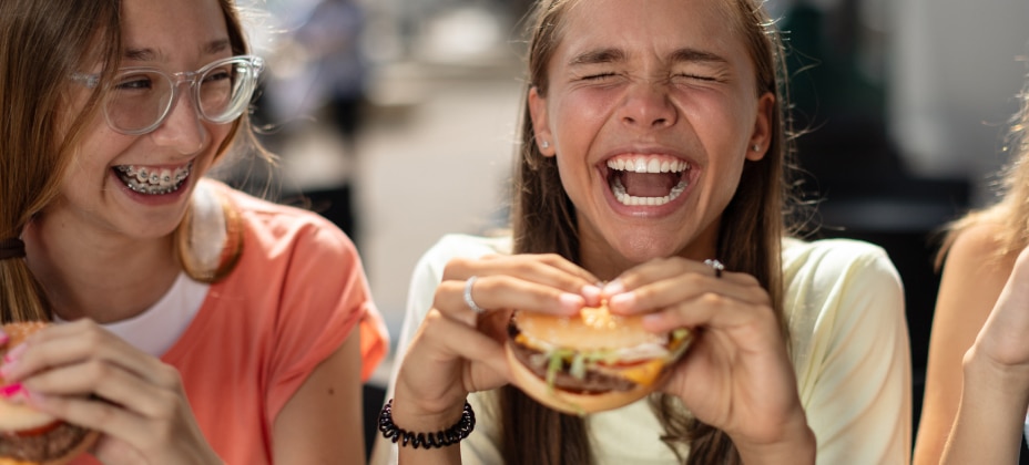 Two smiling individuals enjoying burgers together outdoors, sharing a moment of laughter and happiness. No recognizable landmarks or historical buildings are visible.