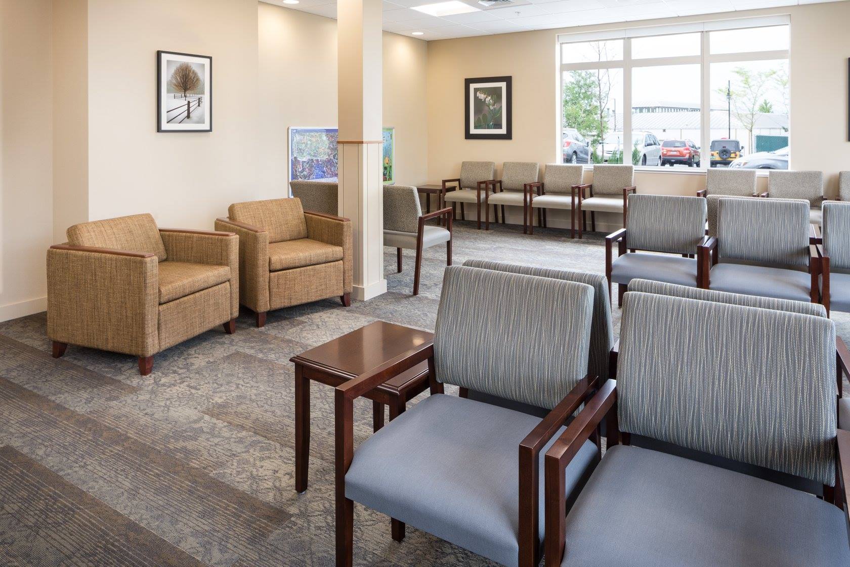 A clean, spacious waiting room with modern chairs, tables, artwork, and large window; ample seating arrangement, neutral tones, bright lighting.