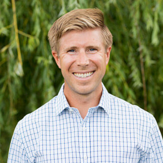 A person in a checkered shirt smiles in front of lush green foliage, with willow leaves hanging in the background.