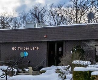 A snow-covered building with the address "60 Timber Lane" appears, surrounded by leafless trees and a satellite dish on the roof.